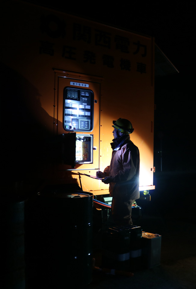 暗闇の中、高圧発電機車の計器を監視する作業員