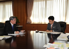 【枝野経済産業大臣（右）に実施計画を報告する当社八木社長（左）】